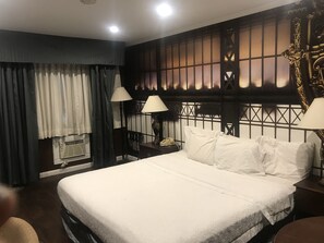 A hotel room with a large bed, two bedside lamps, a nightstand with a telephone, and a decorative headboard.