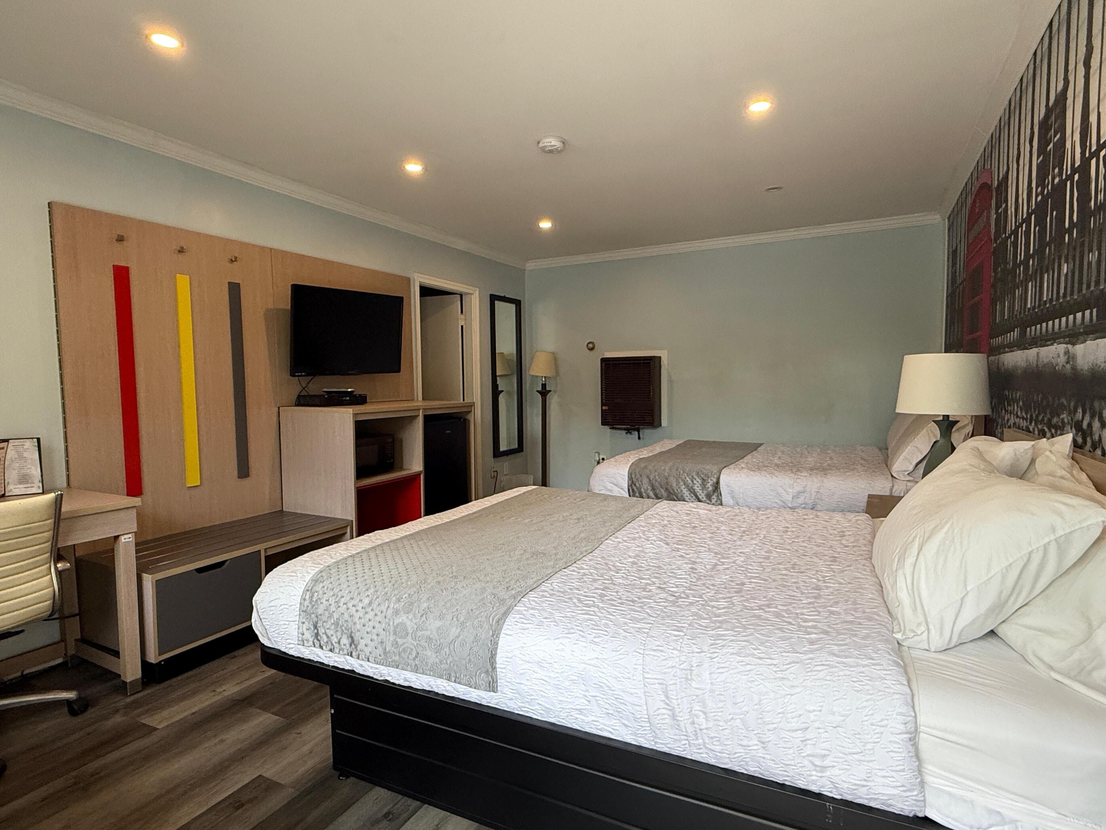 Una habitación de hotel con dos camas, un escritorio, un televisor y un espejo grande.