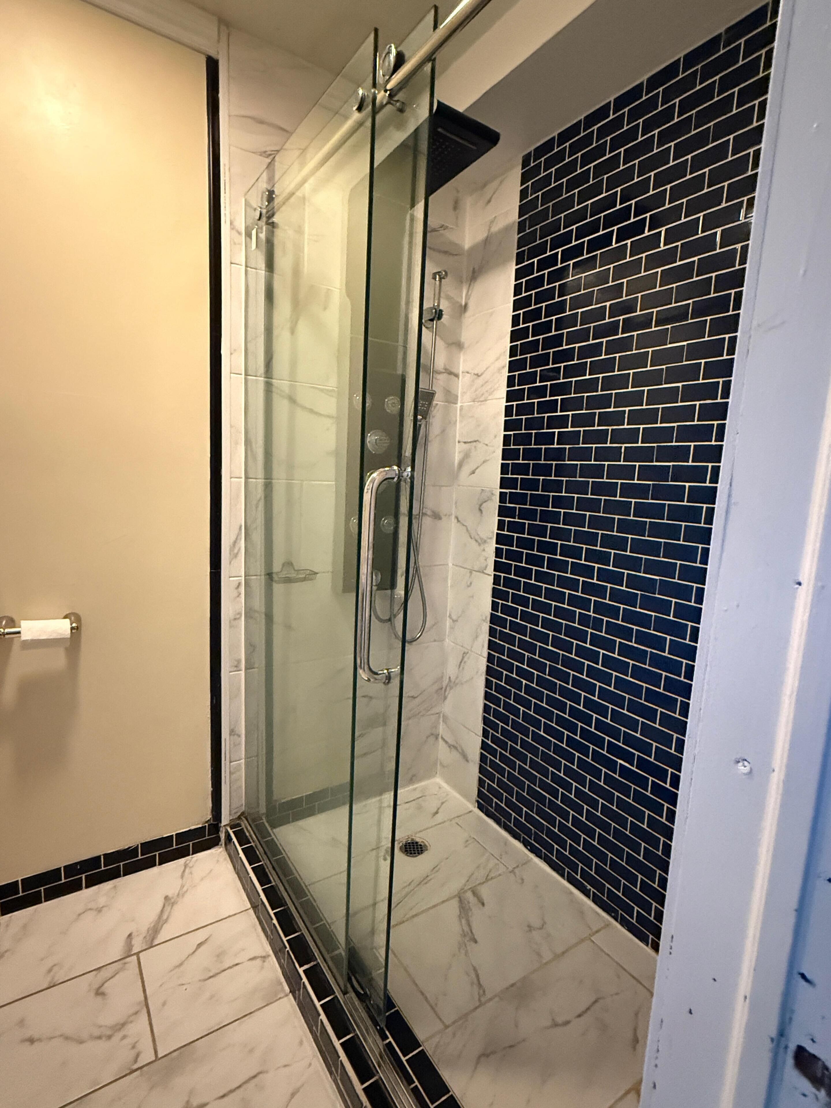 Um chuveiro com paredes de vidro, chão de mármore e parede revestida de azulejos pretos.