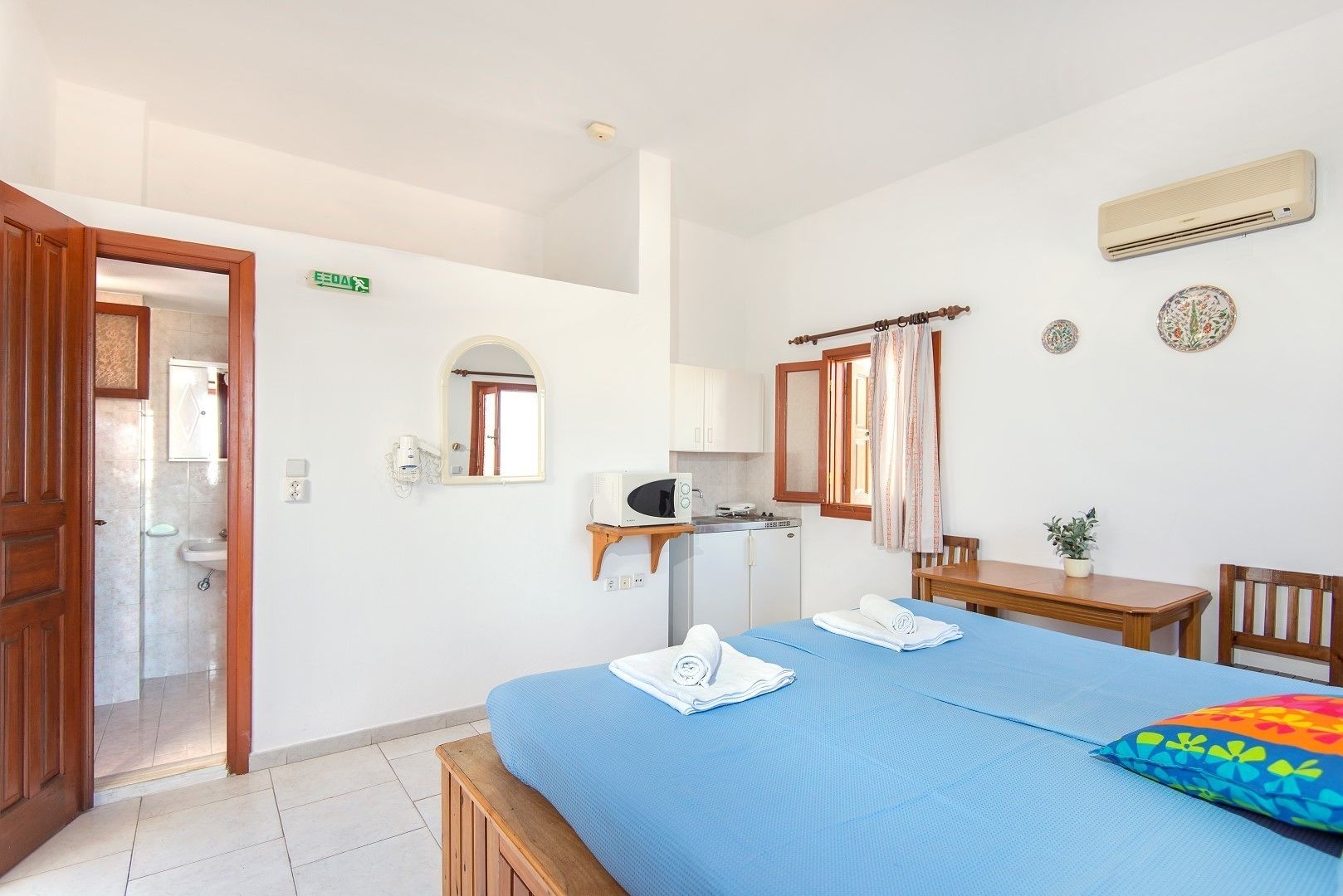 A hotel room with a bed, a desk, a chair, a microwave, a small table, and a window with curtains.