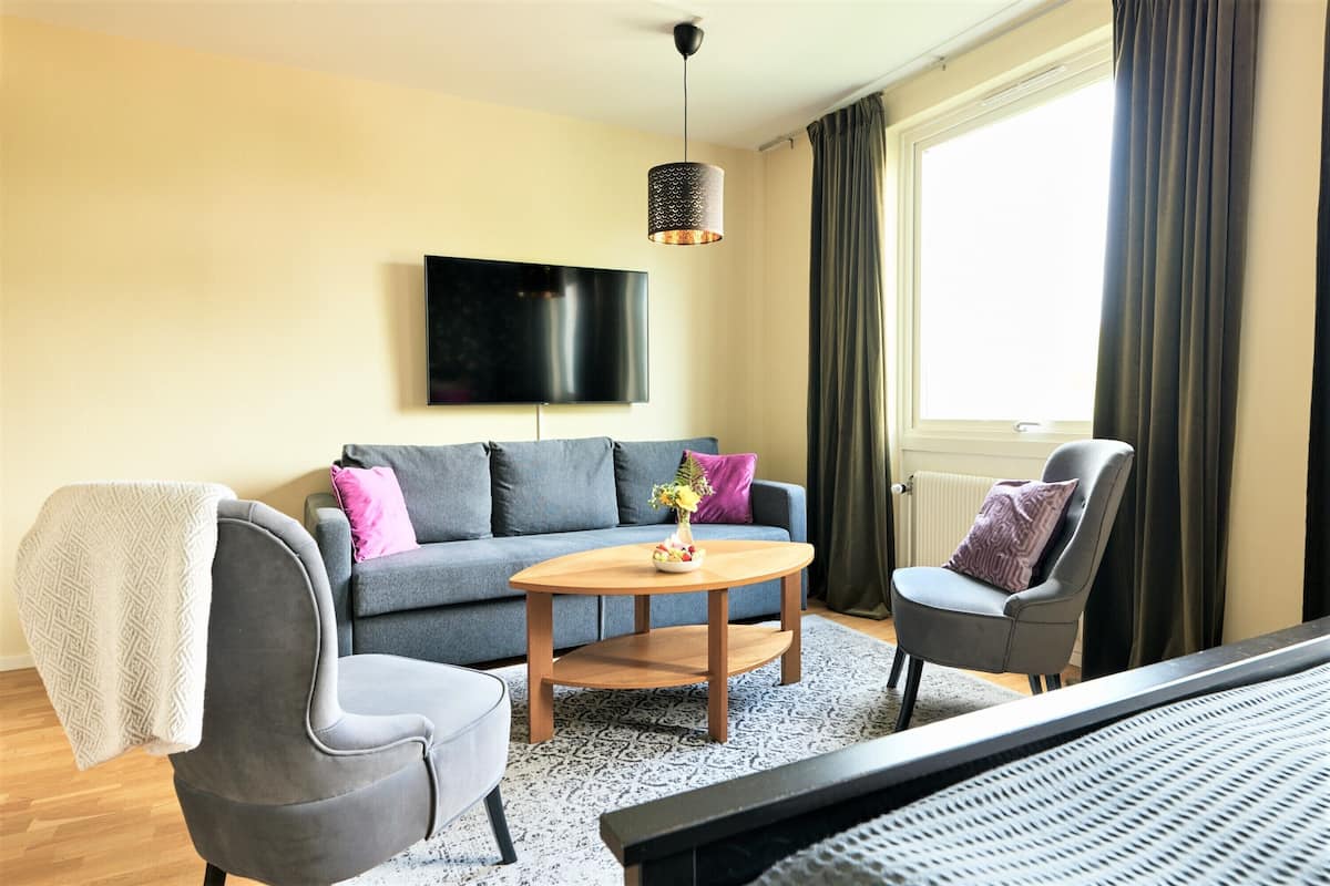 A modern living room with a grey sofa, a wooden coffee table, a grey armchair, and a TV mounted on the wall.