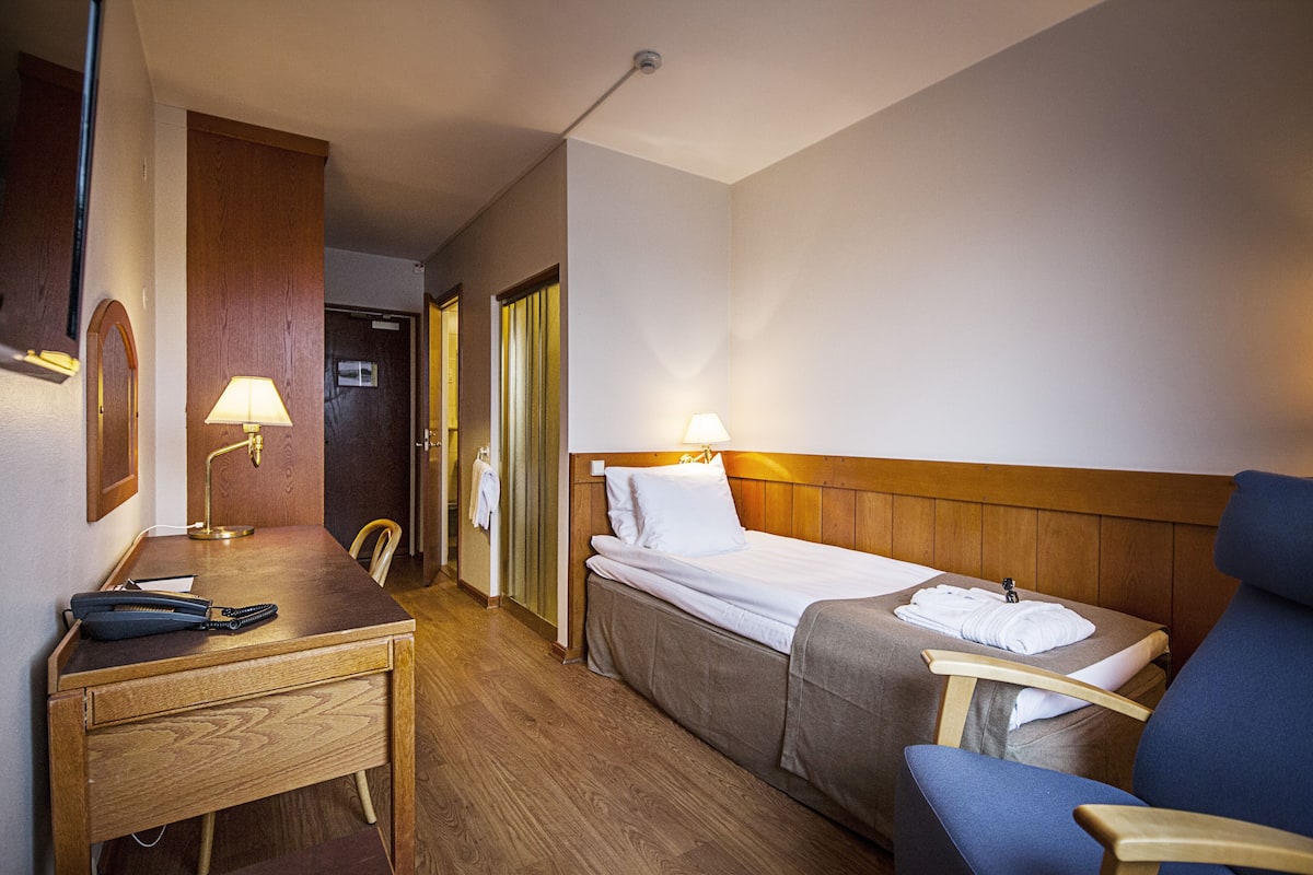A hotel room with a wooden desk, two single beds, a chair, and a mirror.
