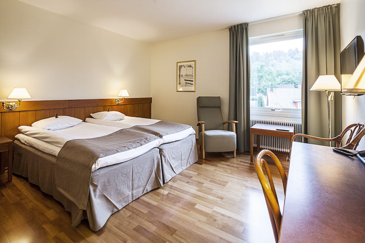 A hotel room with a double bed, a chair, a table, and a view of the outdoors.