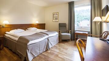 A hotel room with a double bed, a chair, a table, and a view of the outdoors.