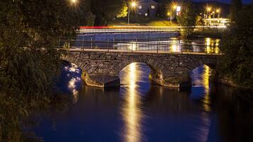 A stone bridge over a calm river at night with streetlights reflecting on the water.
