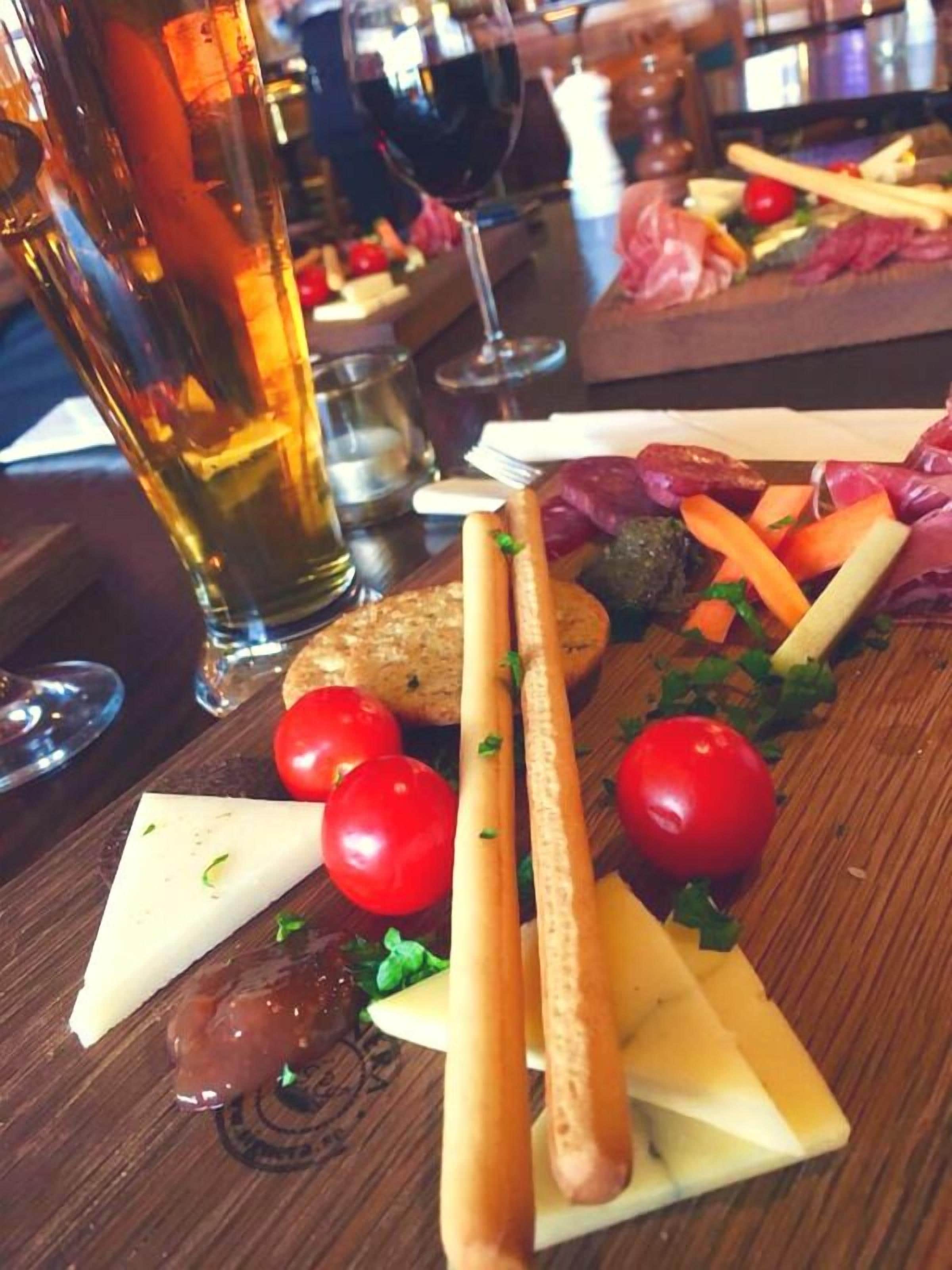 A charcuterie board with various cheeses, tomatoes, and breadsticks on a wooden table.