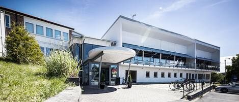 Un edificio moderno con entrada cubierta, zona de estacionamiento y bicicletas aparcadas afuera.