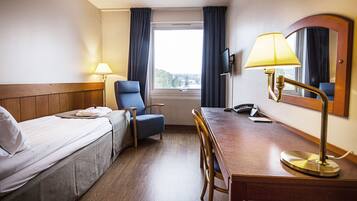 A hotel room with a bed, a desk, a chair, a lamp, a television, and a window with curtains.