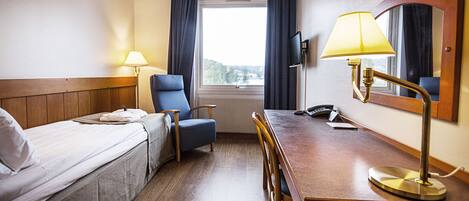 Habitación de hotel con cama, escritorio, silla, lámpara, televisor y ventana con cortinas.