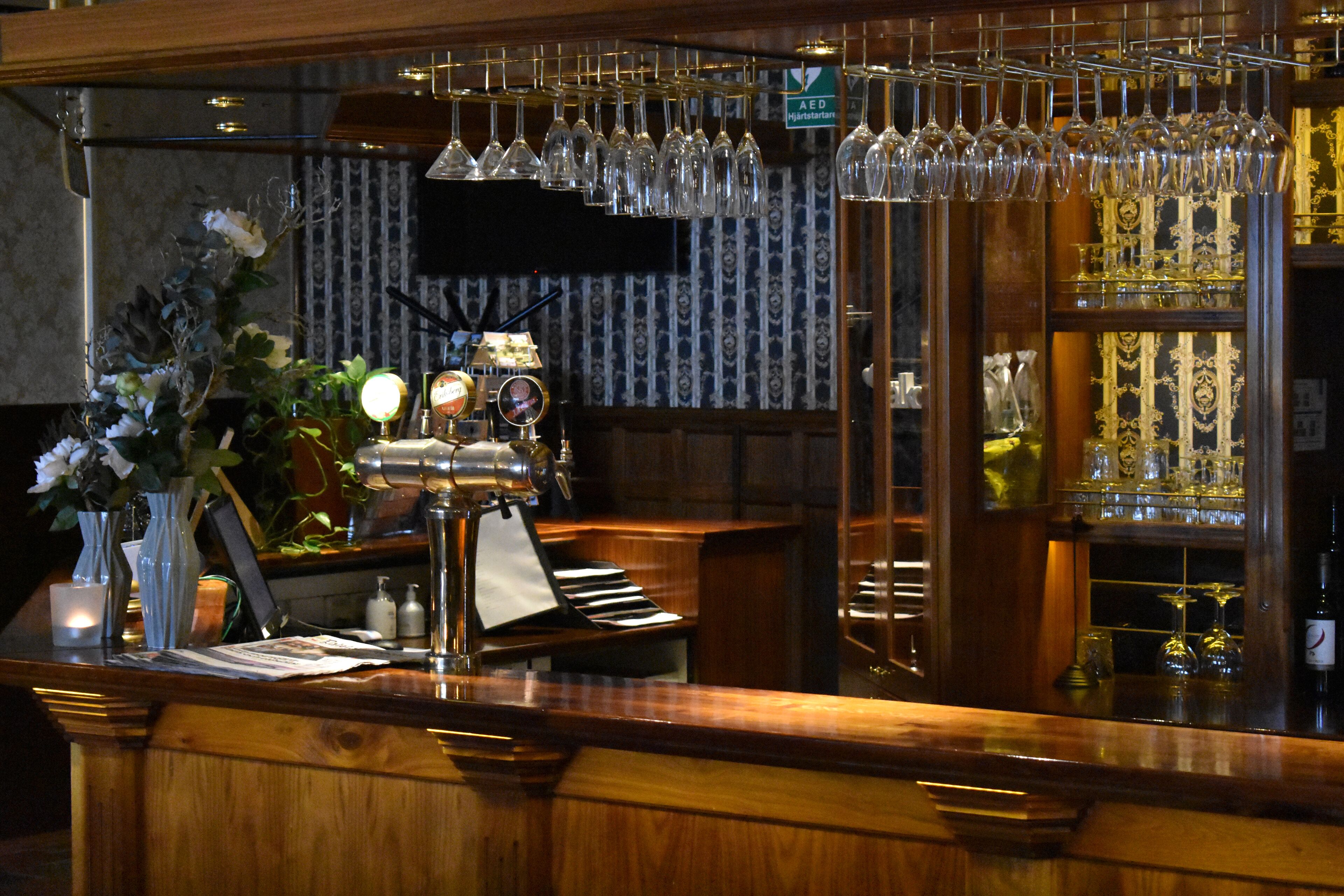 Zona de bar con mostrador de madera, copas de vino colgantes y un piano.