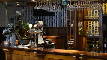Zona de bar con mostrador de madera, copas de vino colgantes y un piano.