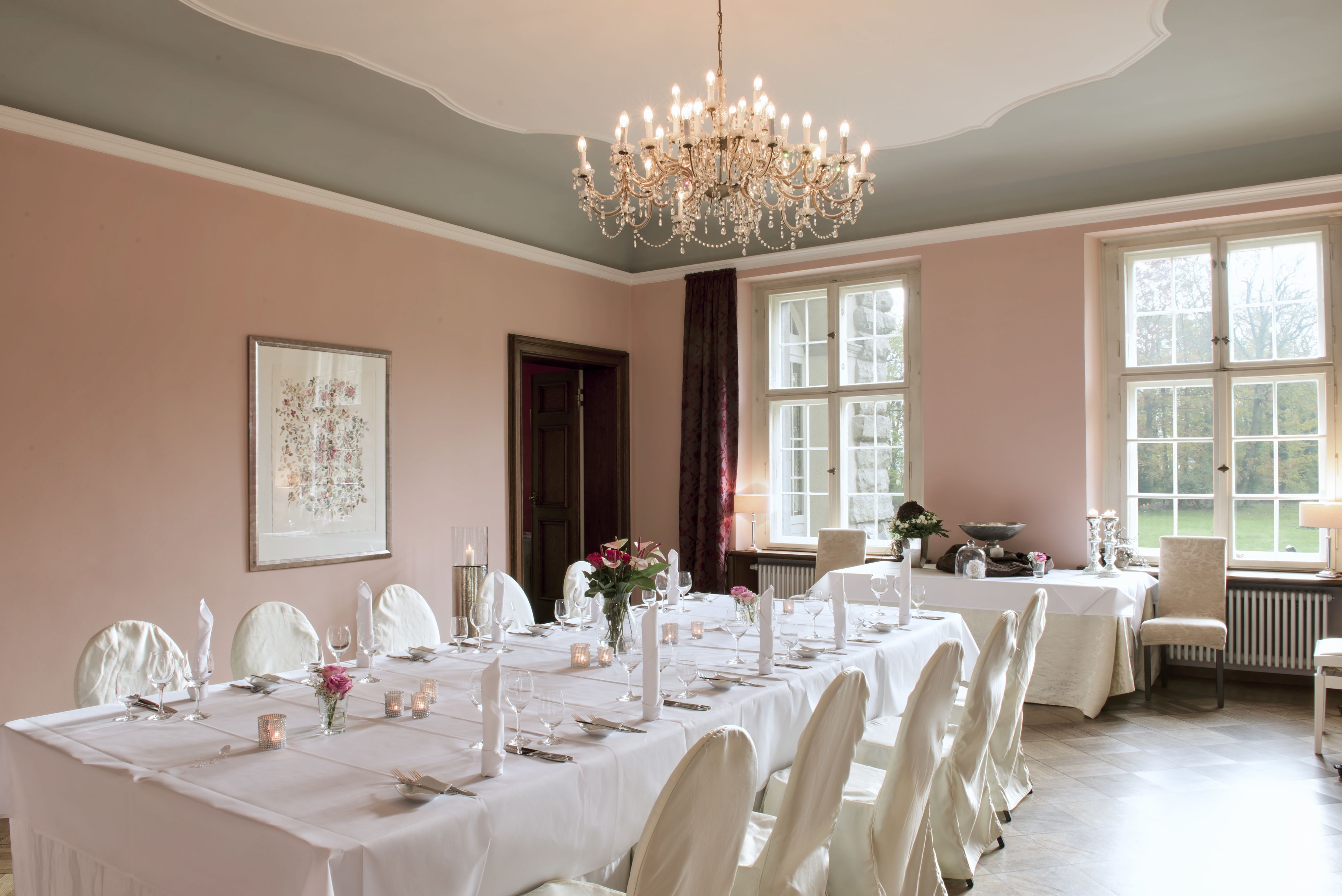 Une salle à manger avec un lustre, des nappes blanches et des chaises.