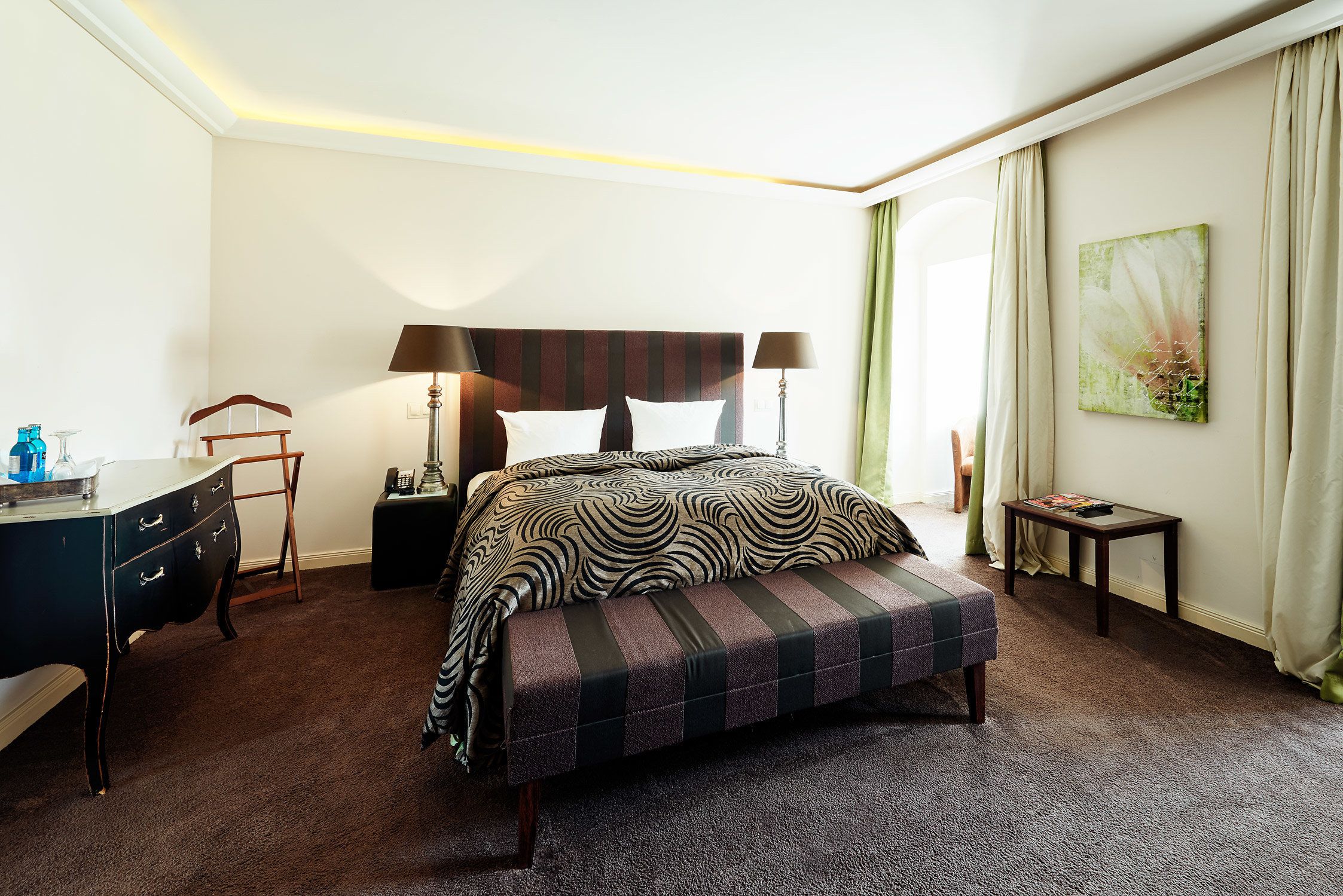 A hotel room with a large bed, bedside tables, a desk, and a bench.