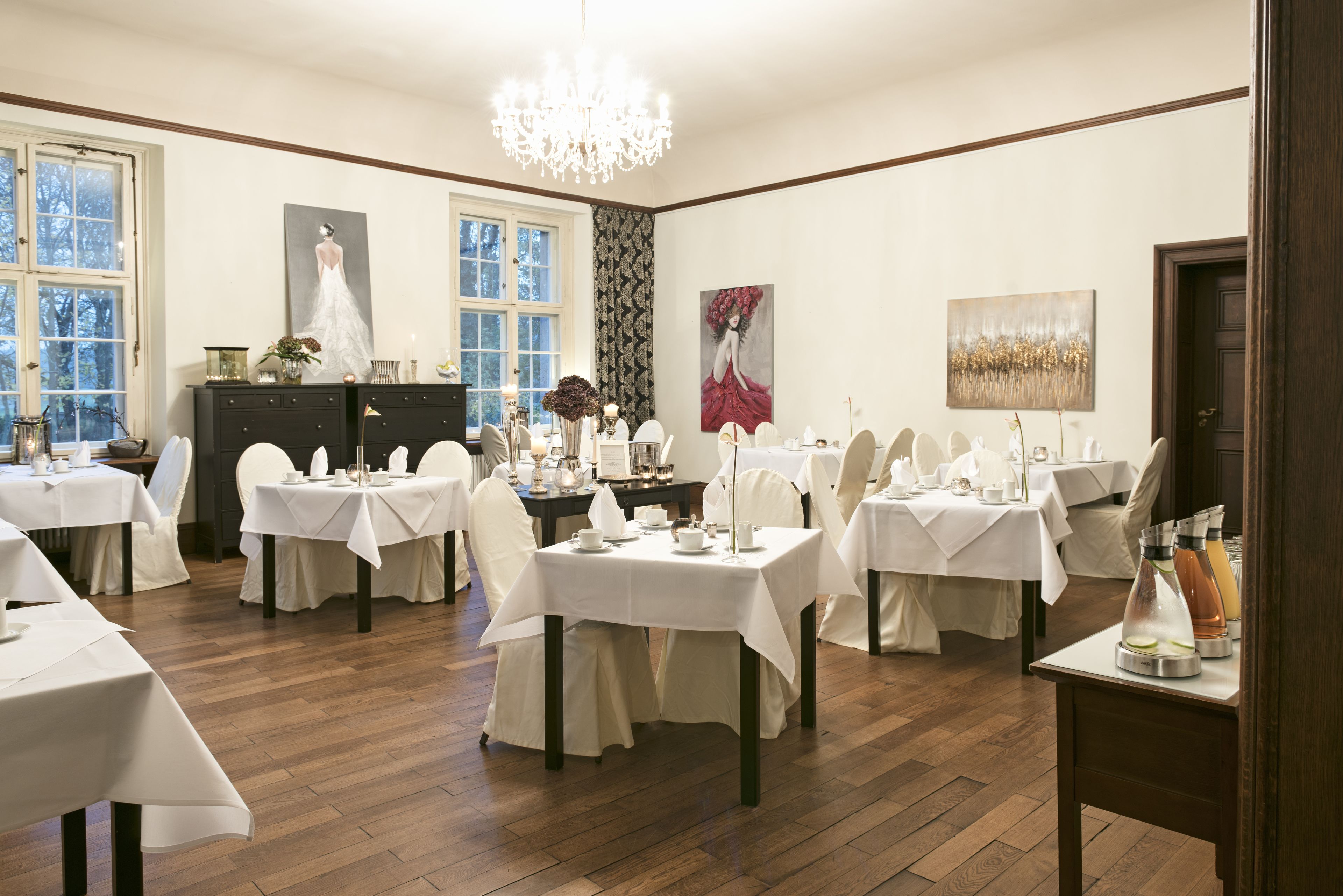 A dining area with multiple tables set for service, a chandelier, and artwork on the walls.