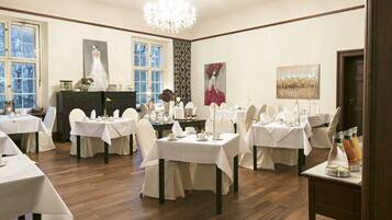 A dining area with multiple tables set for service, a chandelier, and artwork on the walls.