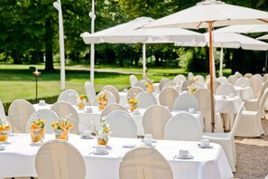 An outdoor event with round tables covered in white tablecloths, white chairs, and white umbrellas. - Schloss Kartzow (Potsdam)
