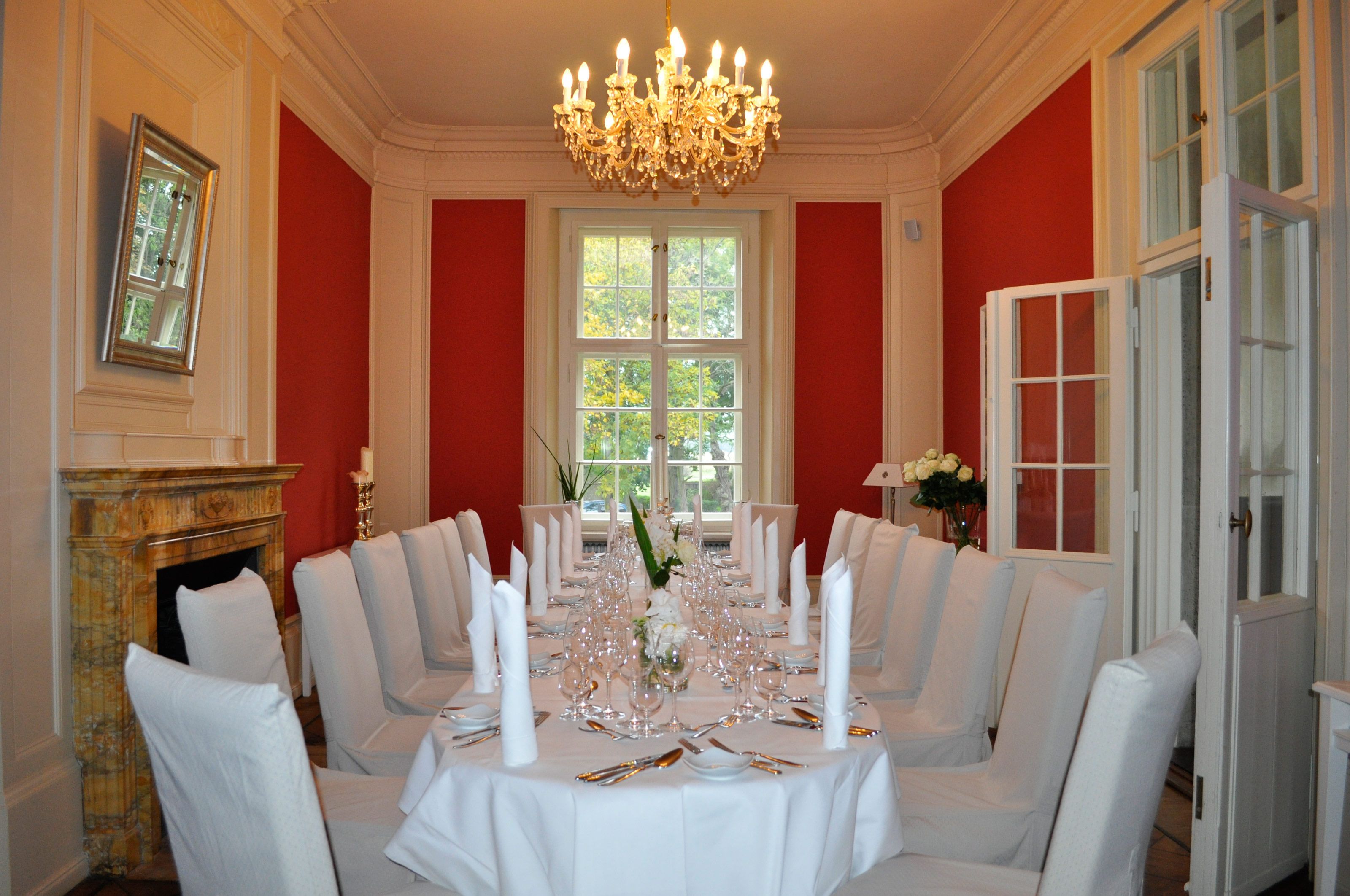 A formal dining room with a long table set for a meal, a chandelier, and a fireplace.