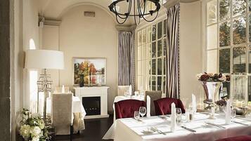 A formal dining room with a fireplace, elegant table settings, and large windows.