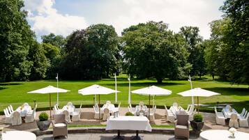 An outdoor dining area with tables and chairs, umbrellas, and a well-maintained lawn.