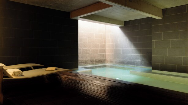 A spa room with a wooden bench, a glass-enclosed hot tub, and a stone wall. - 9Hotel Sablon (Brussels)
