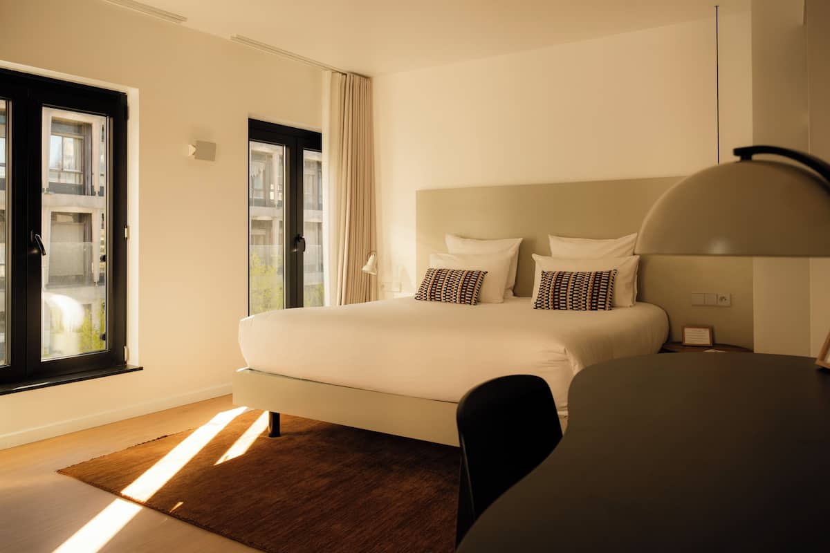 A modern hotel room with a large bed, a desk, and a view through a window.
