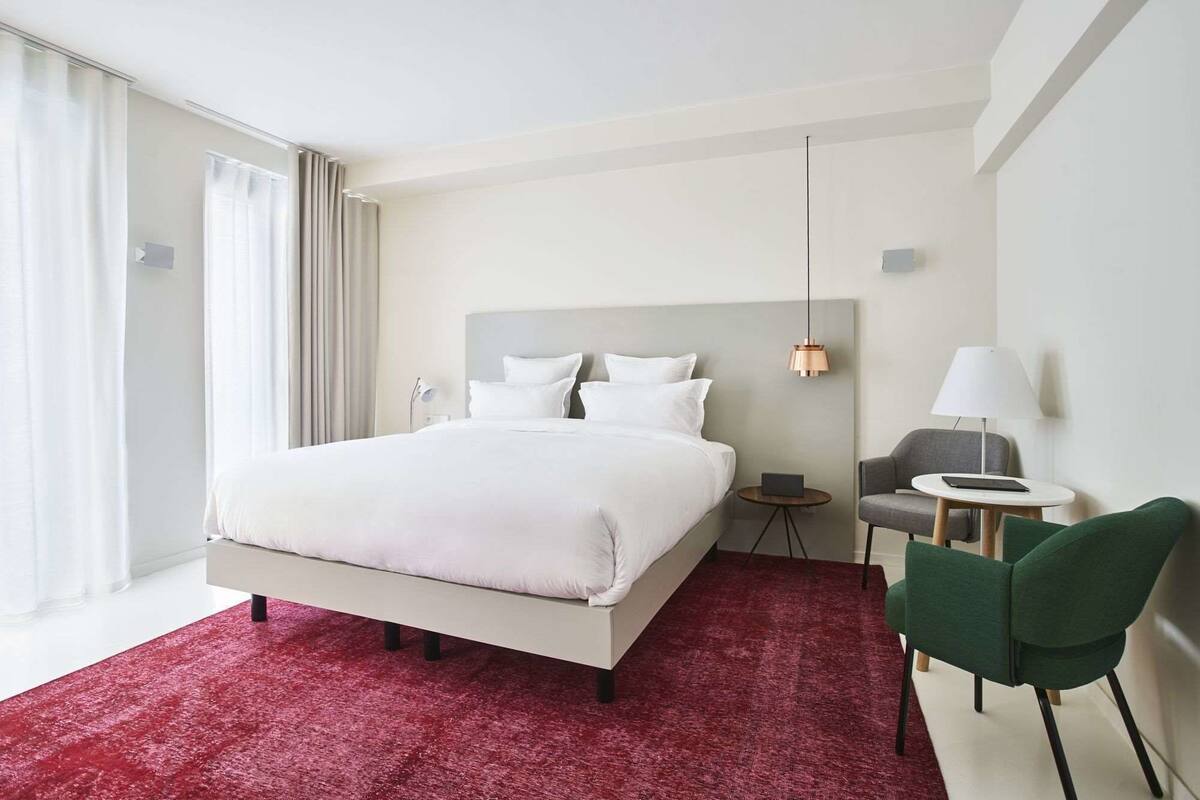 A hotel room with a large bed, a desk, a chair, a lamp, and a view of the outdoors.