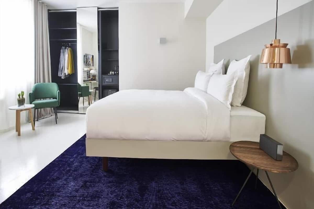 A bedroom with a large bed, a small side table, a chair, a desk, and a wardrobe.