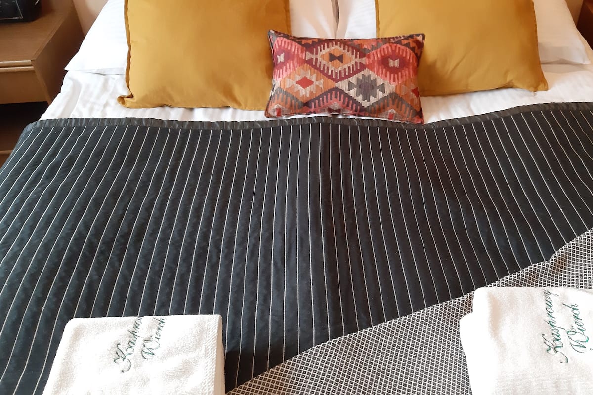 A neatly made bed with striped bedding, a patterned pillow, and two towels with embroidered text.