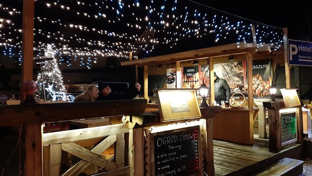 Een houten terras met daarboven lichtslingers, een kerstboom en een bord voor een restaurant.