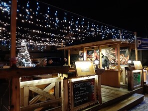 A wooden outdoor seating area with string lights overhead, a Christmas tree, and a sign for a restaurant. - Resort Kasprowy Wierch (Zakopane)