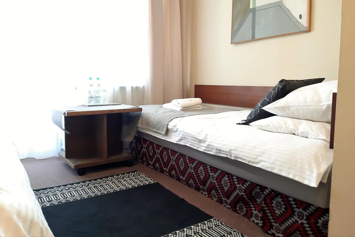 A hotel room with a bed, a bedside table, a mirror, and a window with curtains.