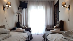 Een hotelkamer met twee bedden, een televisie, een lamp en uitzicht op het groen.