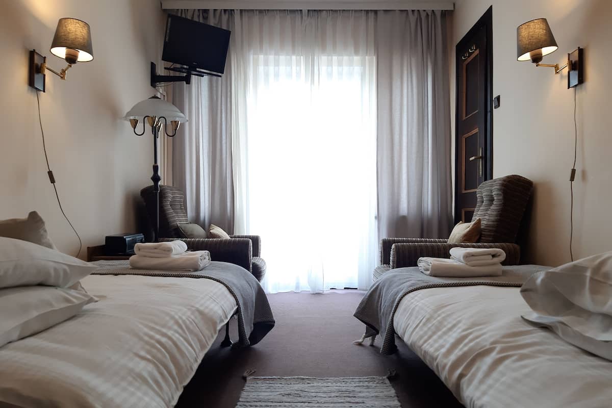 A hotel room with two beds, a television, a lamp, and a view of the outdoors.