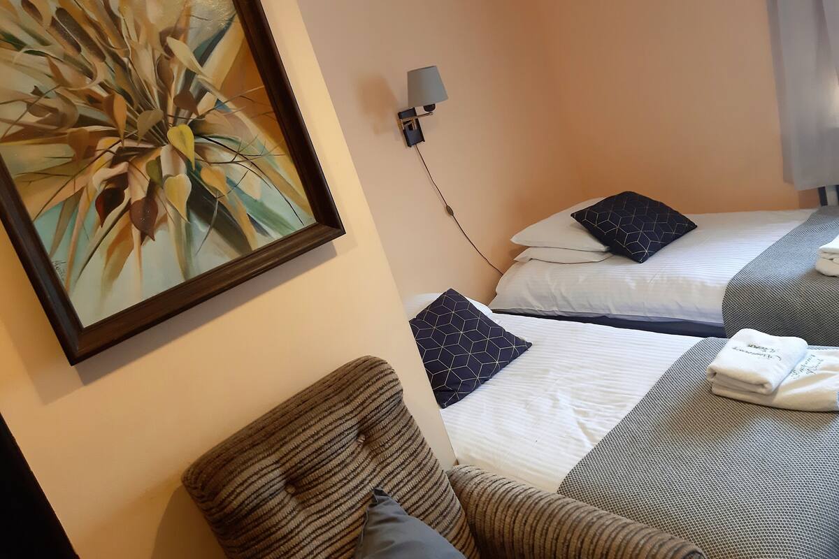 A hotel room with two beds, a painting on the wall, a lamp, and a chair.