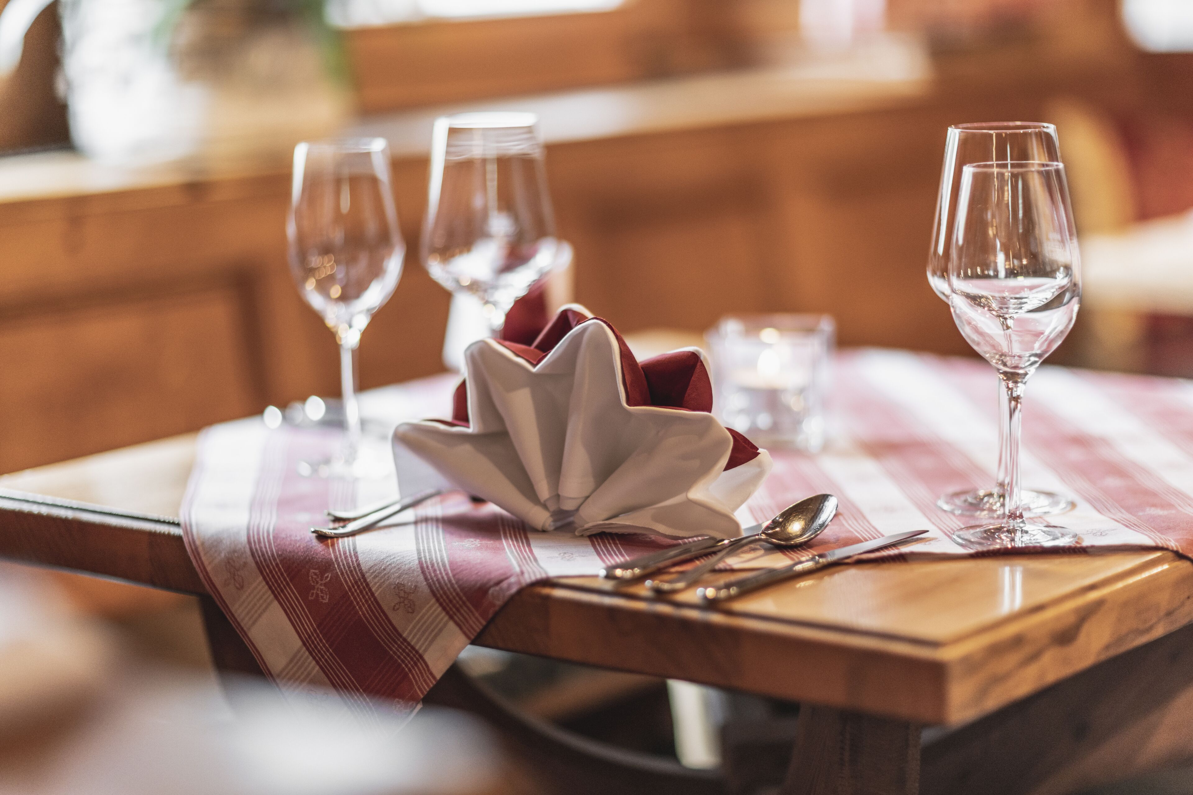 A dining table with a red and white striped tablecloth, a white ceramic centerpiece, and three wine glasses.