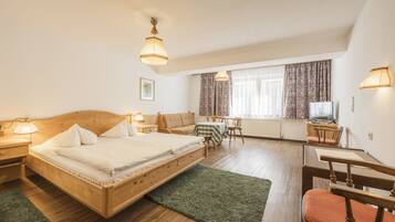 A bedroom with a wooden bed, a desk, a chair, a sofa, and a television.