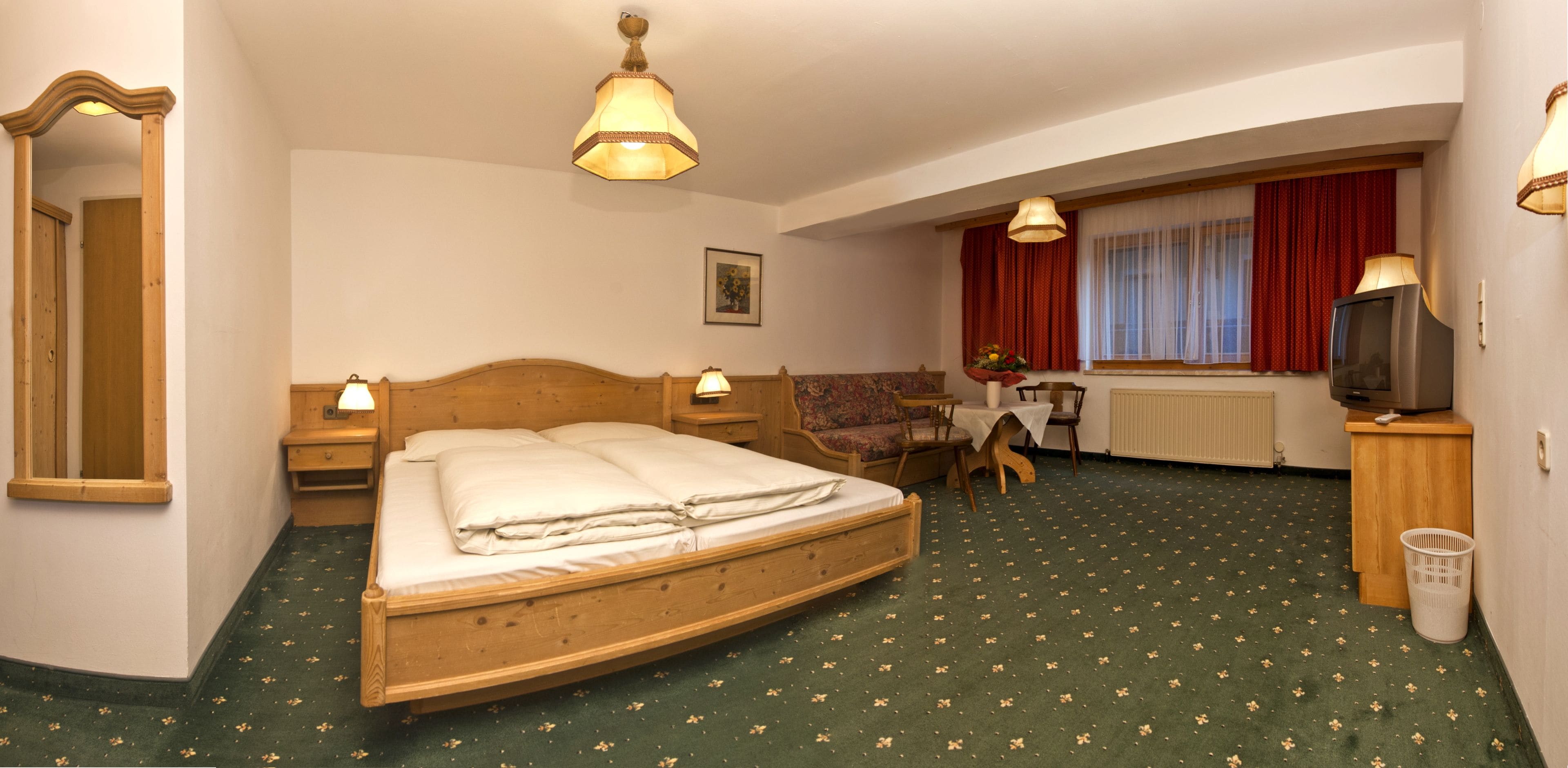A hotel room with a wooden bed, a desk, a chair, a television, and a window with curtains.