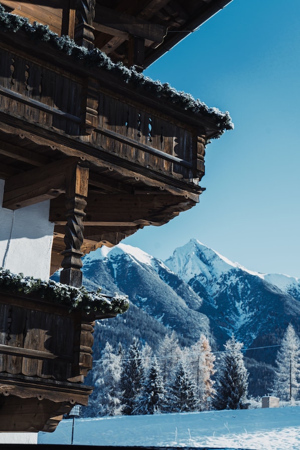 A wooden chalet with multiple balconies, set against a snowy mountain backdrop.
