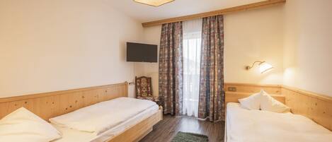 A bedroom with two single beds, a television on the wall, a wooden headboard, and a window with curtains.