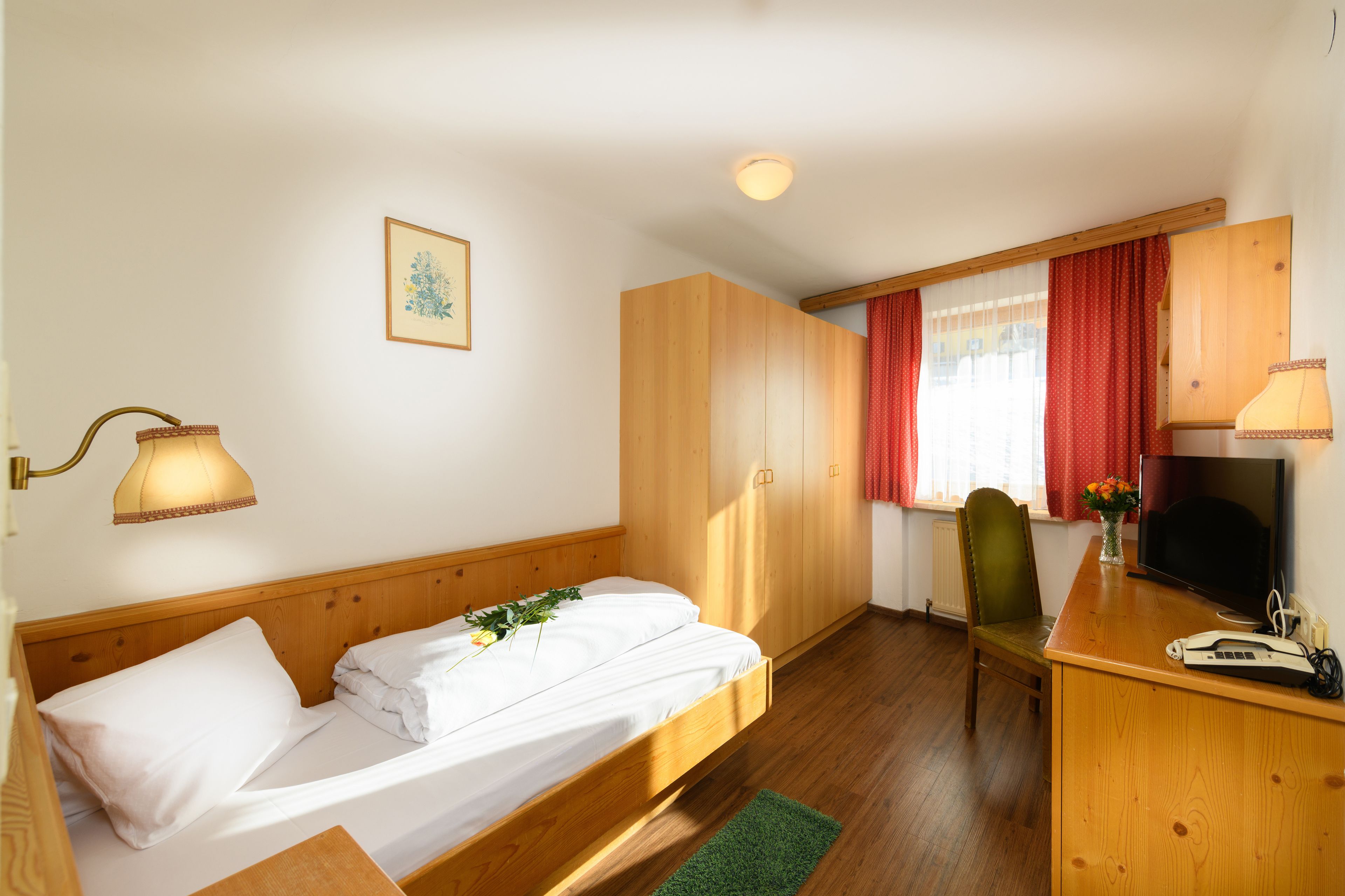 Una habitación con cama, escritorio, silla, televisor y lámpara.
