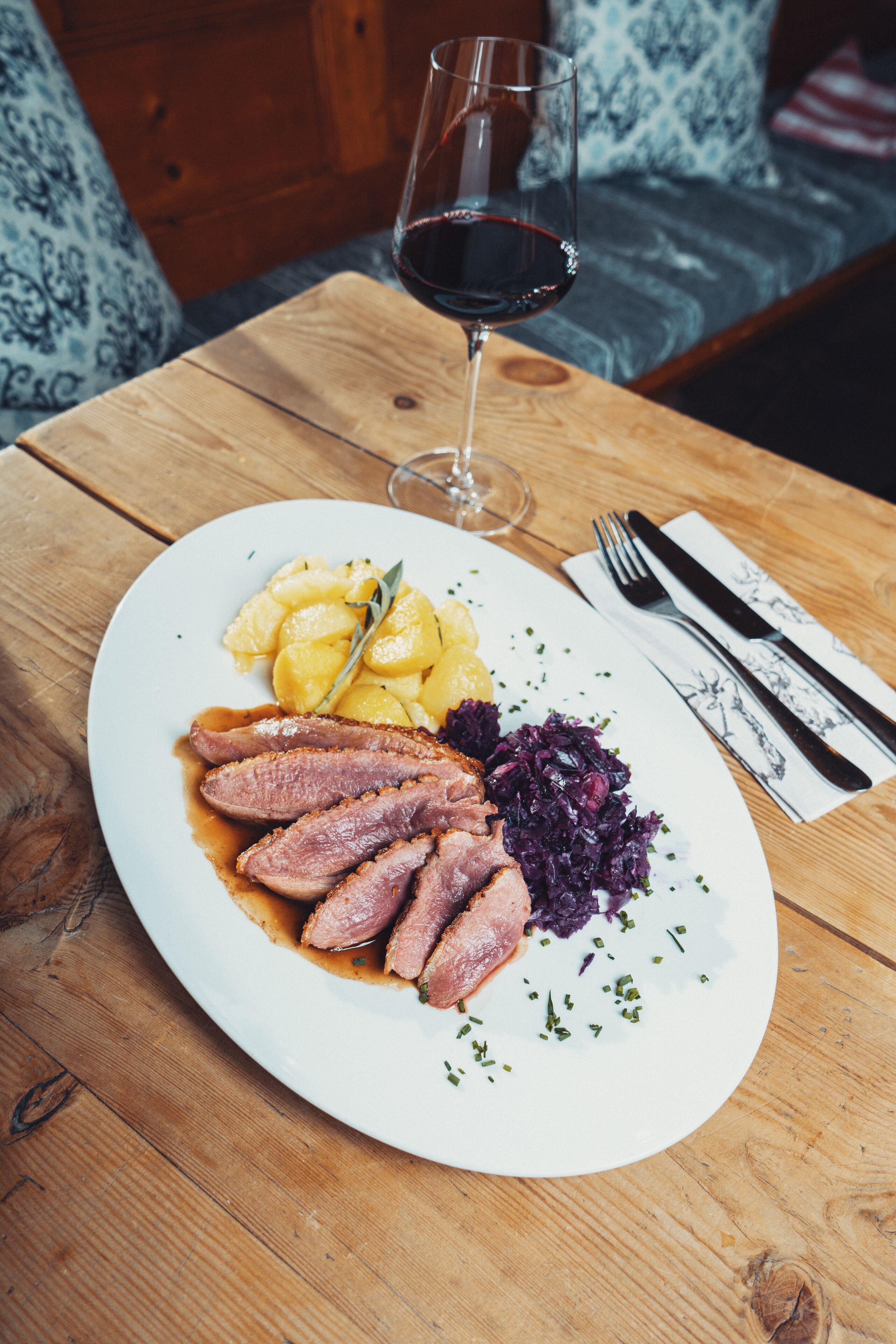Un plato de comida con patatas, col roja y pato sobre una mesa de madera.