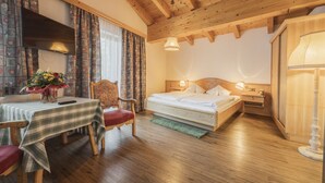 A cozy room with a wooden ceiling, a bed with a nightstand, a table with chairs, and a TV mounted on the wall. - Gasthof Batzenhaeusl (Seefeld in Tirol)