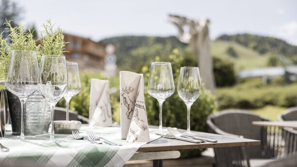 A table set outdoors with wine glasses, a vase with greenery, and a napkin with a deer design. - Gasthof Batzenhaeusl (Seefeld in Tirol)