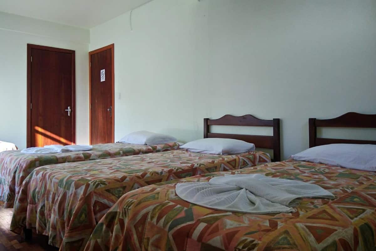 Une chambre avec deux lits simples, chacun doté d’une tête de lit en bois et d’une couvre-lit à motifs. On y trouve une porte avec une pancarte et un luminaire au plafond.