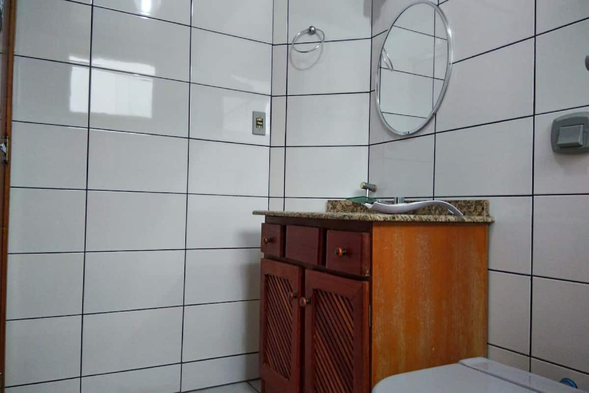 Une salle de bain avec des murs carrelés de carreaux blancs, un meuble en bois avec un lavabo et des toilettes.
