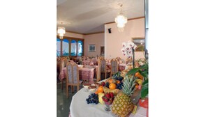 Un espace repas avec des tables rondes recouvertes de nappes roses, des chaises en bois et une variété de fruits et de légumes disposés sur les tables.