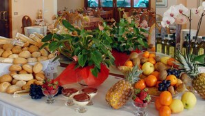 Une table de buffet proposant divers aliments, notamment des fruits, du pain et des desserts, dans une pièce meublée de meubles en bois et dotée d’un grand miroir qui reflète l’ensemble de la pièce.