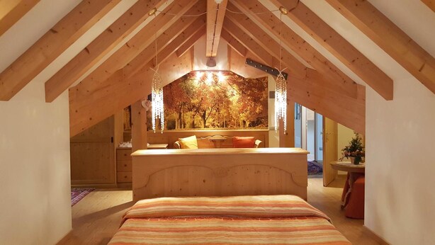 Une chambre mansardée chaleureuse avec un plafond en pente, un lit en bois, un banc et une vue sur les arbres par la fenêtre.