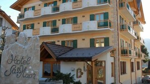Un hôtel à plusieurs étages doté de balcons, une petite annexe avec un toit en pente et une enseigne indiquant « Hôtel SassMaor ».
