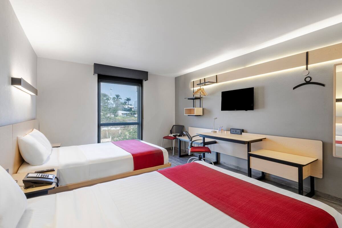 Ett modernt hotellrum med två sängar, ett skrivbord, en stol, en TV och ett stort fönster.